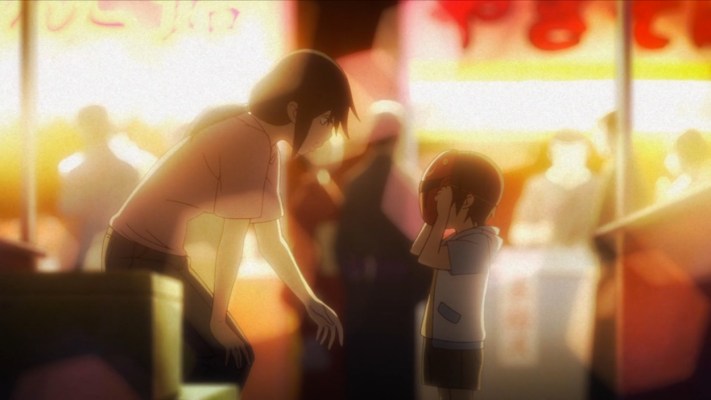 Little Satoru as a young boy putting on a superhero mask. His mother is leaning down in front of him. Brightly lit festival booths are in the background.